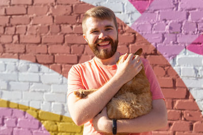 Portrait of smiling young man holding brick wall