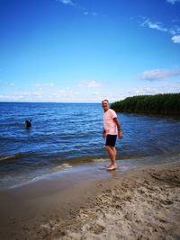 Portrait of mature man standing at beach against blue sky