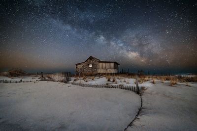 House on snow covered landscape against sky at night