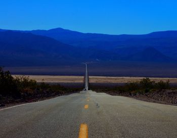 Empty road leading towards mountains against blue sky