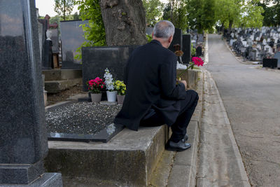 Mature man in black clothes on cemetery, holding a flower and mourning for family loss. 