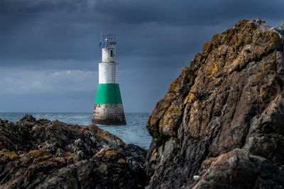 Lighthouse on rock by sea against sky