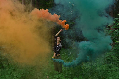 Woman standing by color smoke in forest