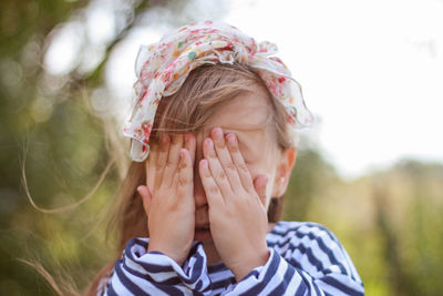 Beautiful little girl covers her face with her hand