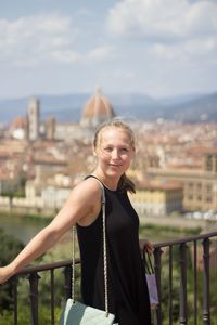 Portrait of smiling woman standing by railing against cityscape