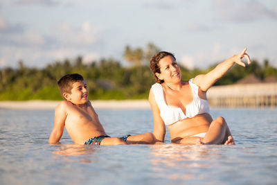 Mother and son sitting on the water of a beach