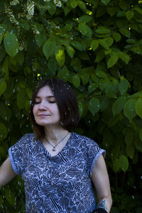 Woman standing with eyes closed against plants during snowfall