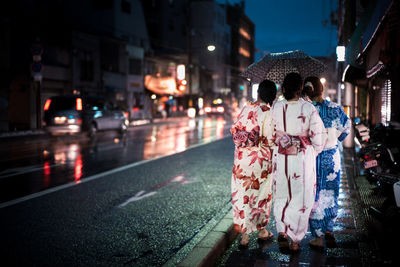 Rear view of women wearing kimonos walking on street at night