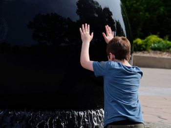 Rear view of boy pushing on built structure at fountain