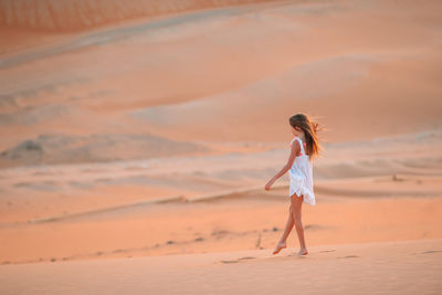 Woman standing on sand at beach against sky during sunset