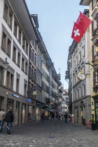 Rear view of people walking on street amidst buildings in city