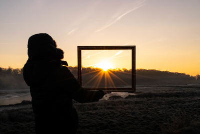 Rear view of silhouette man standing on field against sky during sunset