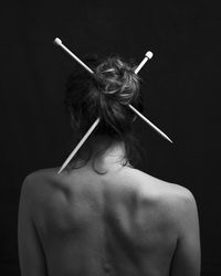 Rear view of shirtless young woman standing against black background