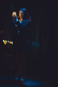 Portrait of beautiful woman holding glowing jar while standing in darkroom at night