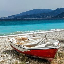 Boat moored on shore by sea against sky