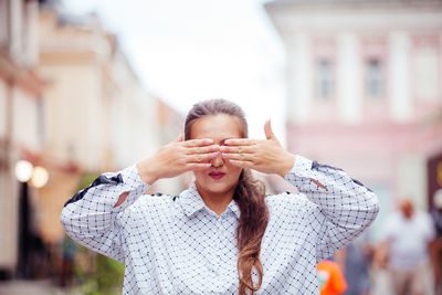 Portrait of young woman with arms raised standing in city