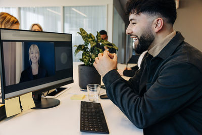 Happy businessman doing video call with female colleague on computer in coworking office