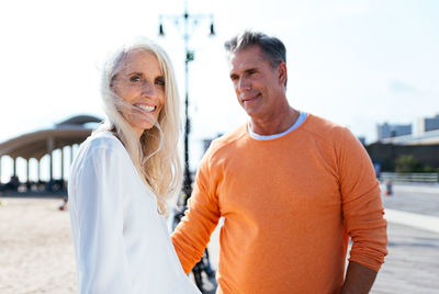 Portrait of smiling senior woman with man standing at beach