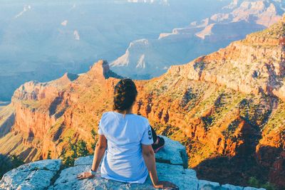 Rear view of woman sitting on cliff against mountains