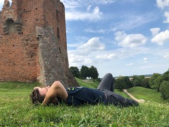 Side view of man lying on grass against sky