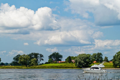 Boat sailing in river by trees against sky