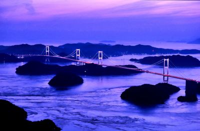 Illuminated bridge over sea against sky at dusk