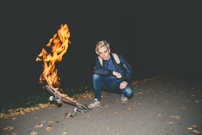 Young man with burning skateboard at night