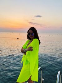 Woman standing in sea against sky during sunset