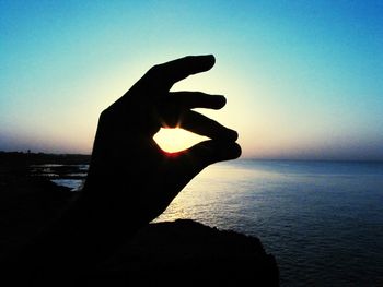 Silhouette of person photographing sunset over sea