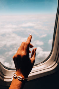 Close-up of hand against sky seen through window