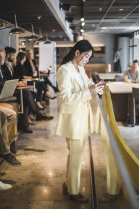 Full length of businesswoman using mobile phone while standing in office