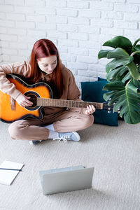 Young man playing guitar while sitting on footpath