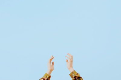 Low angle view of hands against clear blue sky