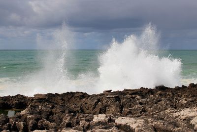 Waves breaking on rocks against the sky