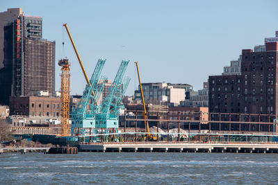 Cranes by buildings against clear sky