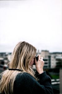 Woman photographing through camera against clear sky