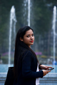 Side view of young woman standing against fountain