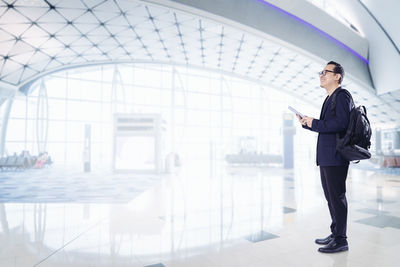 Full length of businessman with backpack using digital table at airport