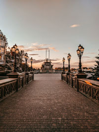 Footpath by street against sky during sunset