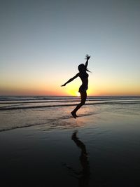 Silhouette woman jumping on beach against sky during sunset