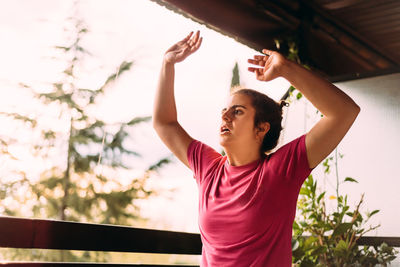 Young woman looking away while standing against tree