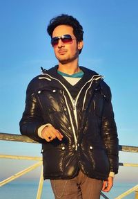 Portrait of young man wearing sunglasses standing against blue sky