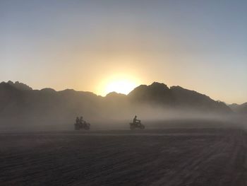 People riding vehicle on land against sky during sunset