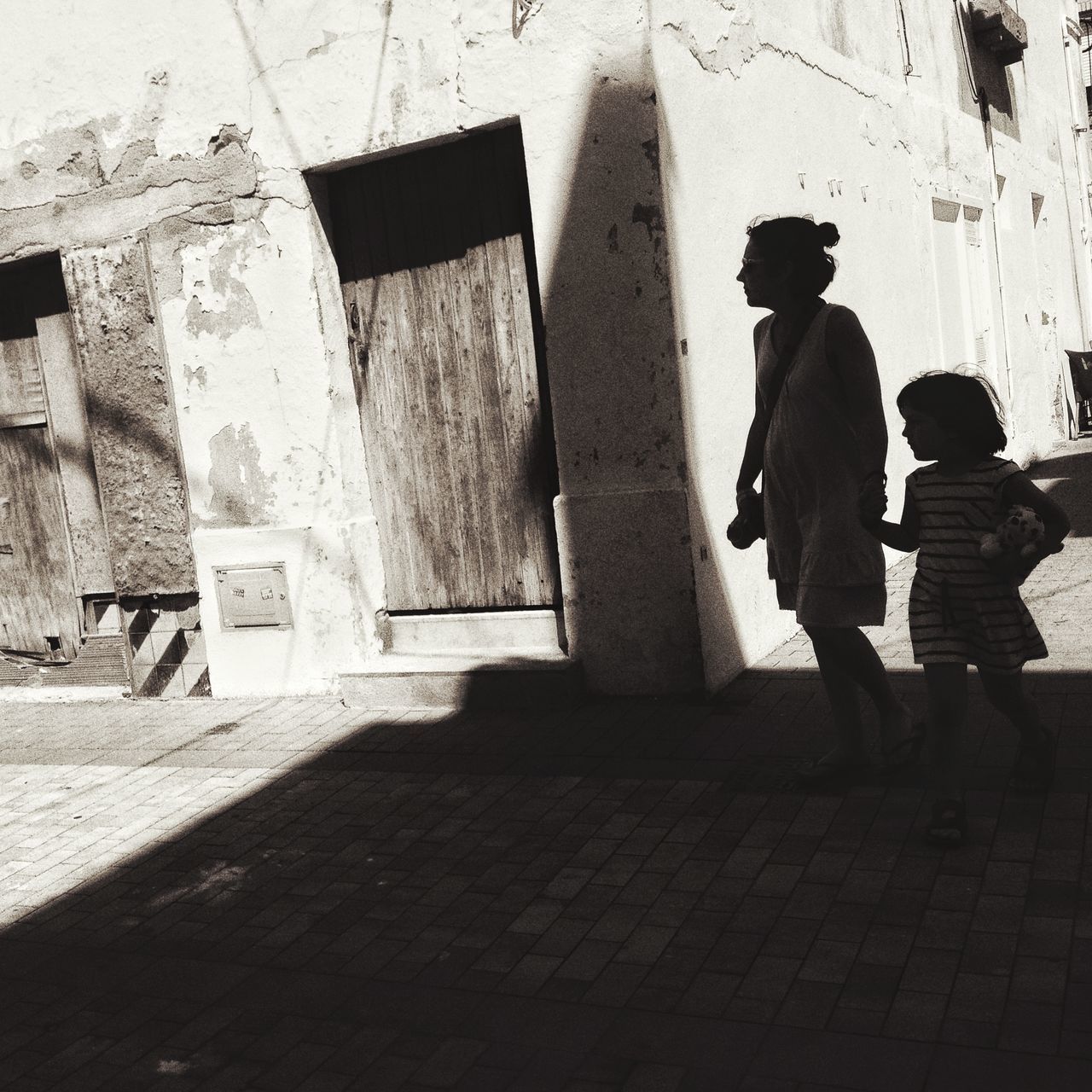 architecture, built structure, building exterior, street, wall - building feature, men, sidewalk, day, shadow, outdoors, wall, rear view, sunlight, building, cobblestone, full length, the way forward, steps, footpath