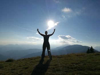 Man with arms outstretched standing on mountain against sky