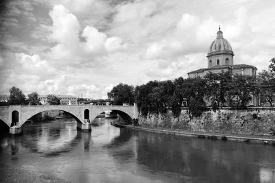 Arch bridge over river against cloudy sky