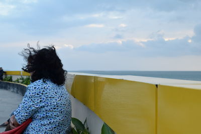 Rear view of woman standing by sea against sky