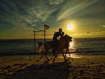 Man riding horse on beach against sunset sky