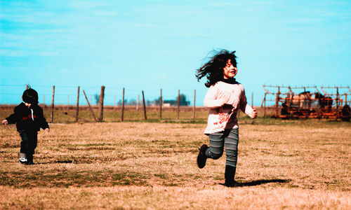 Siblings running on field against blue sky