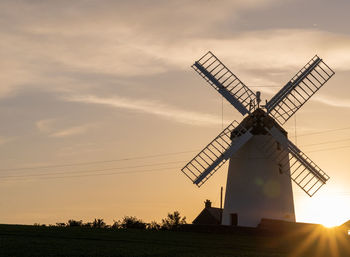 Traditional windmill on field against sky during sunset